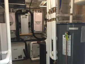 Installed furnace and water heater with white PVC venting and copper piping in mechanical room