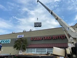 Crane lifting commercial HVAC rooftop unit onto building roof