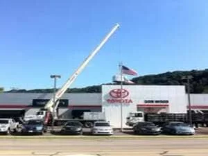 Crane lifting large HVAC ductwork assembly at commercial automotive dealership during installation