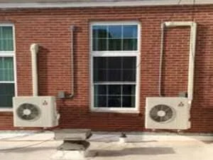 Two white mini-split HVAC condenser units mounted on red brick building exterior
