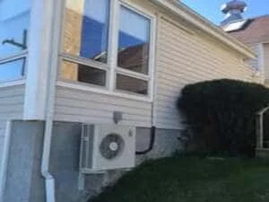 Outdoor AC condenser unit installed on residential home exterior with white siding