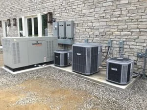 Multiple outdoor AC units installed on gravel pad against stone building exterior