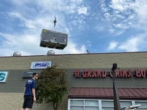 Commercial HVAC unit suspended by crane during rooftop installation on commercial building